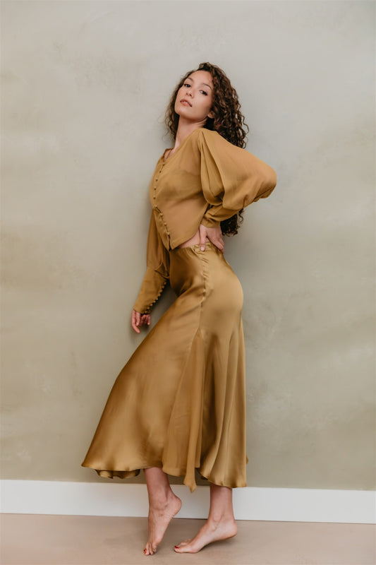Woman wearing a brass top and skirt against a beige wall