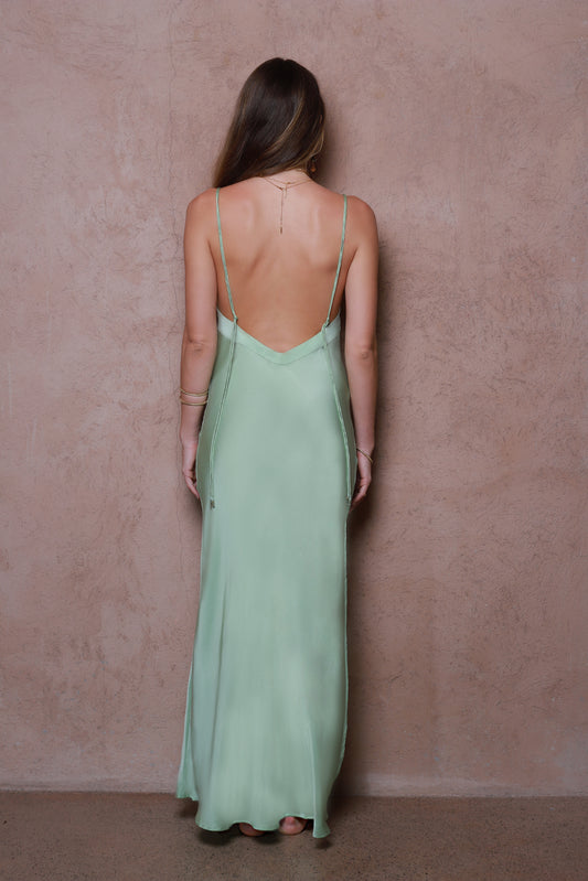Woman wearing a green silk satin dress with thin straps against a pink wall