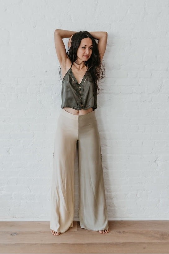 Woman wearing silk embroidery top standing with arms raised against a white brick wall
