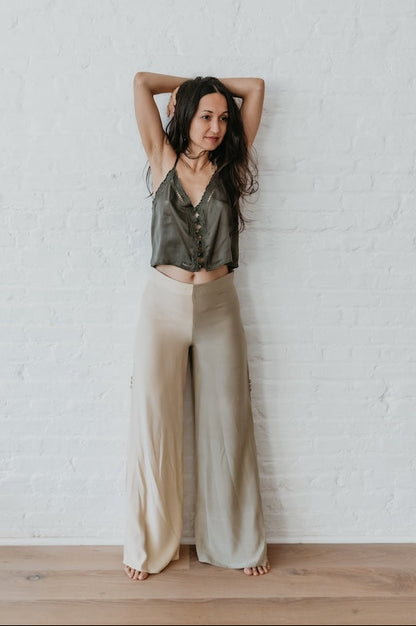 Woman wearing silk embroidery top standing with arms raised against a white brick wall