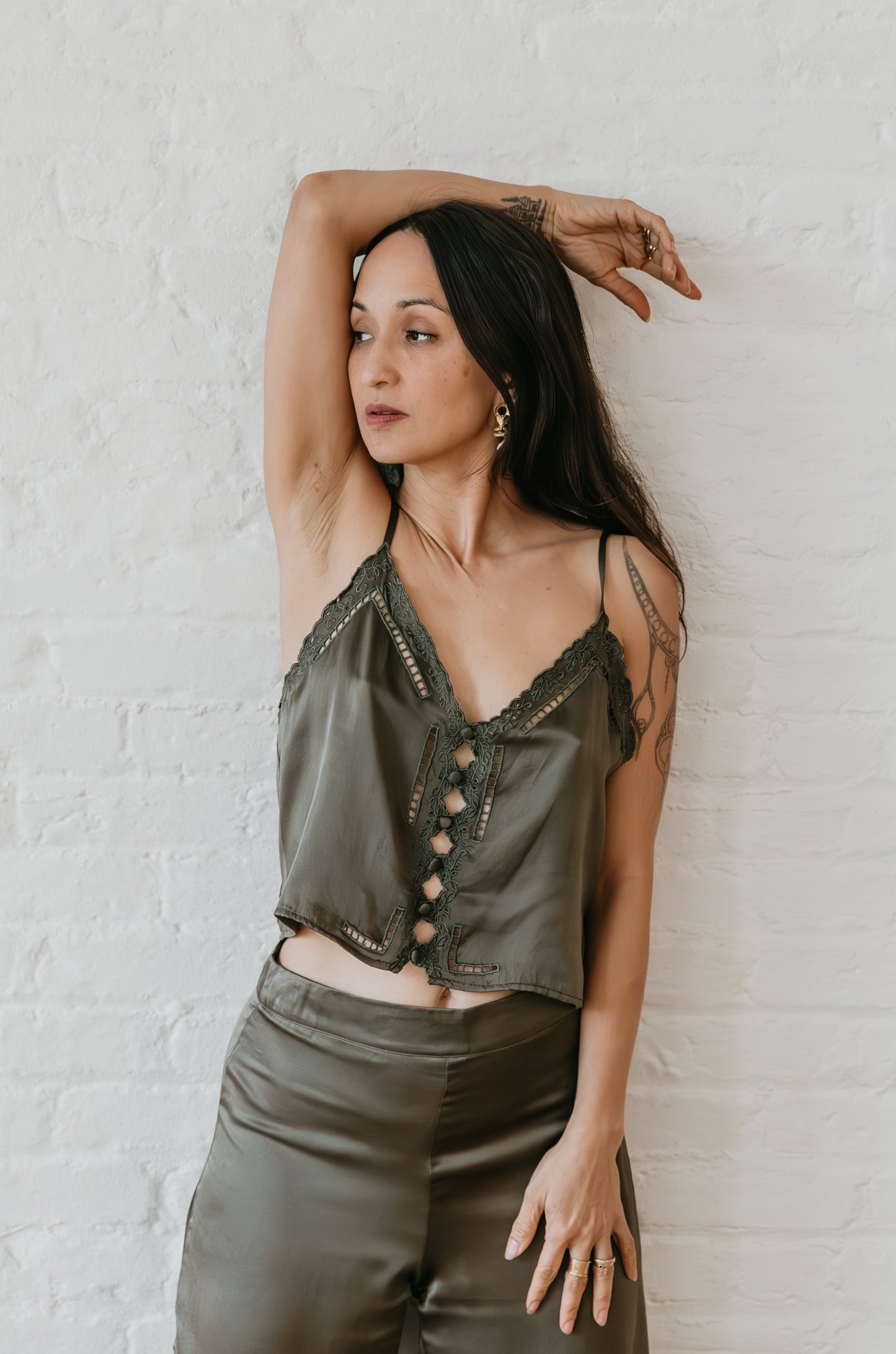 Woman wearing a green  silk satin top and pants against a white brick wall.