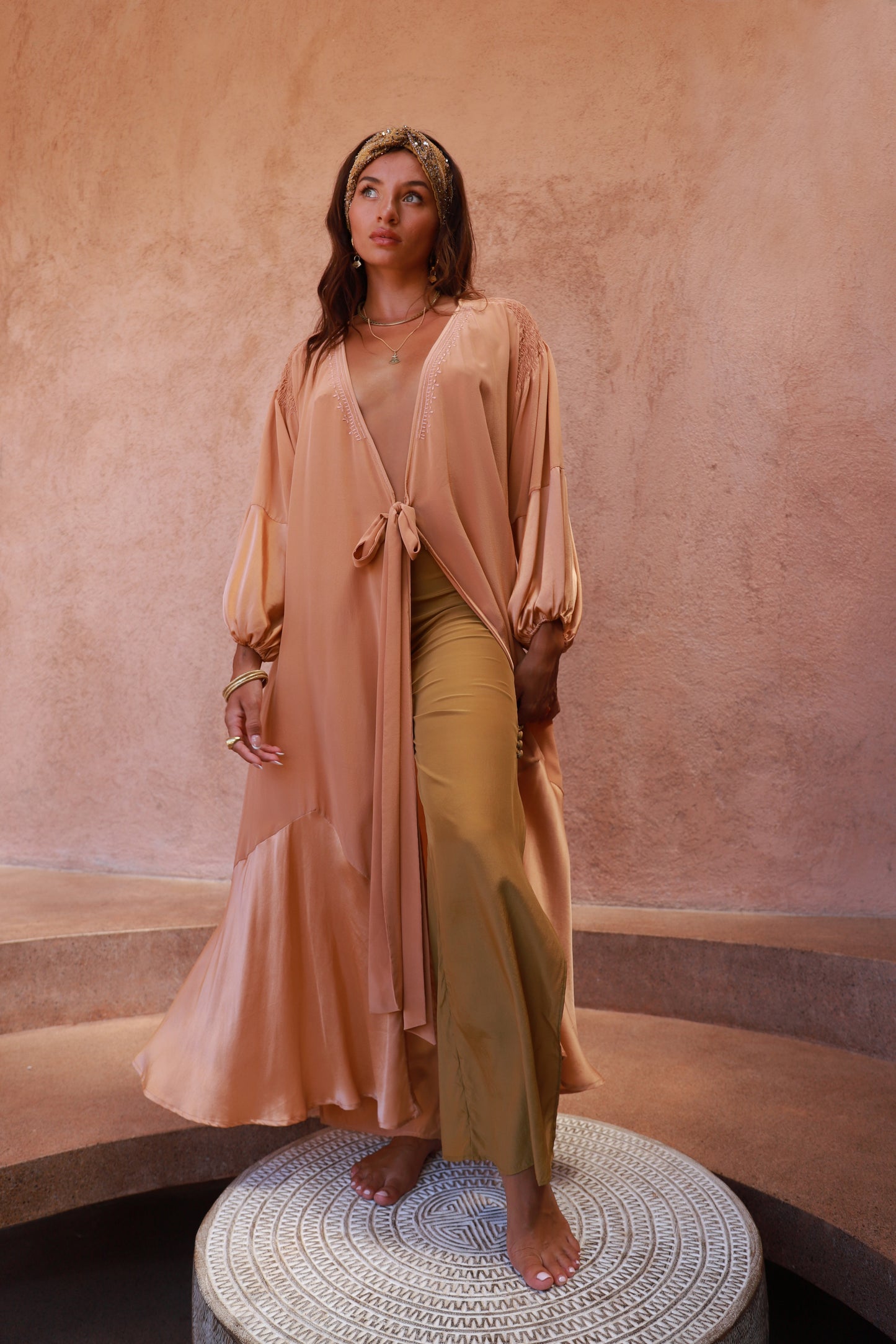 Woman wearing a peach robe and brass pants  with flowing silhouette