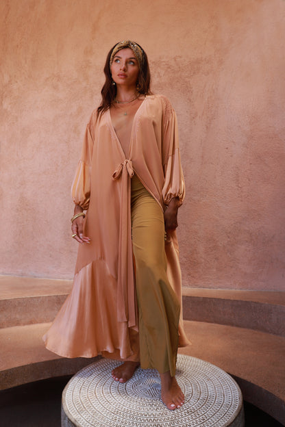 Woman wearing a peach robe and brass pants  with flowing silhouette
