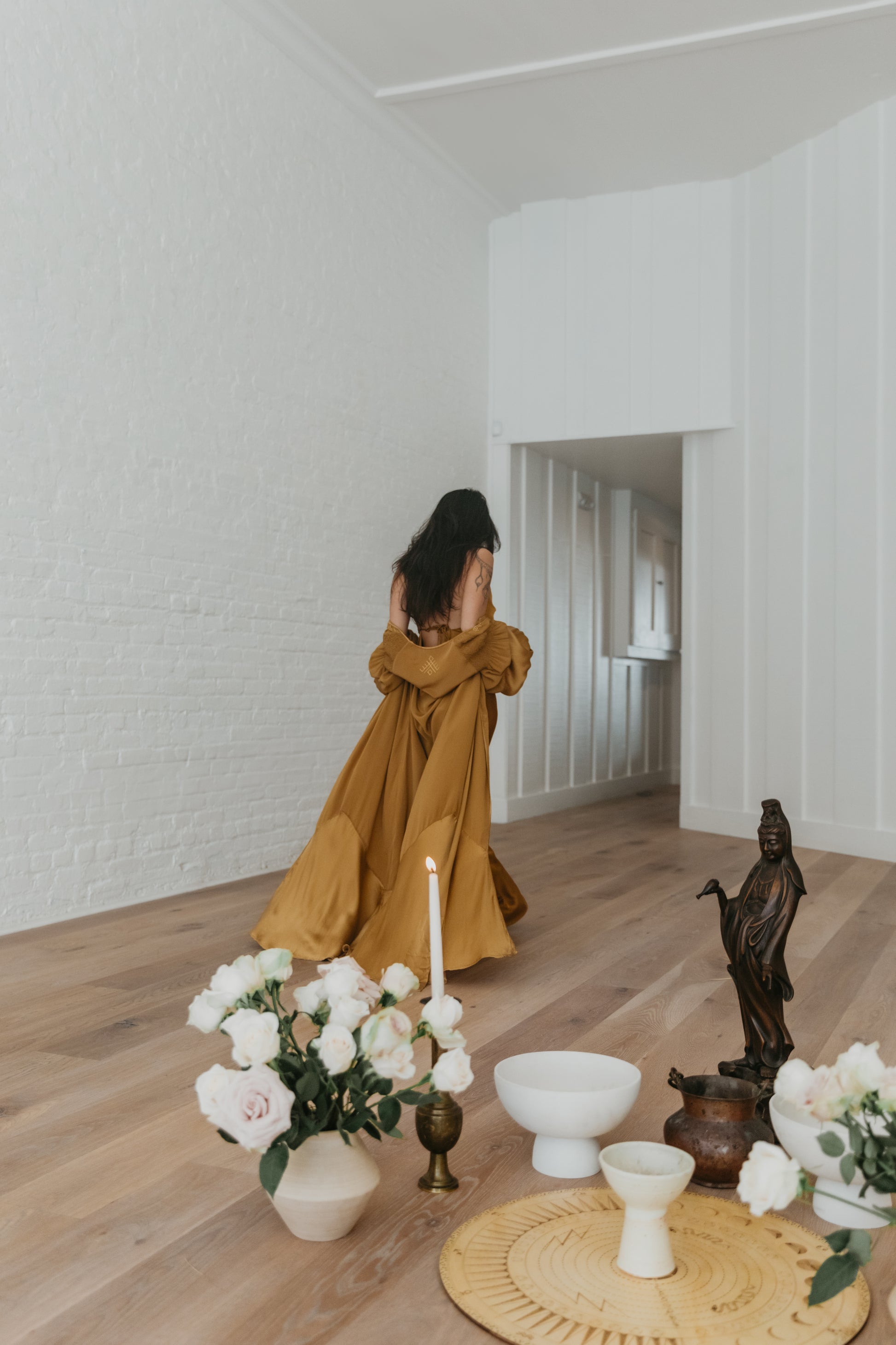 Woman in a brass dress standing in a room with decor items on the floor.