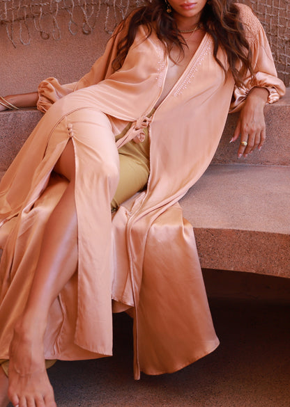 Person wearing a peach satin robe sitting on a stone bench.