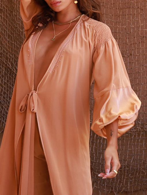 Woman wearing a peach-colored dress with long sleeves against by PAYET Maison