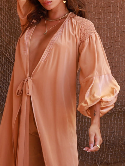 Woman wearing a peach-colored dress with long sleeves against by PAYET Maison