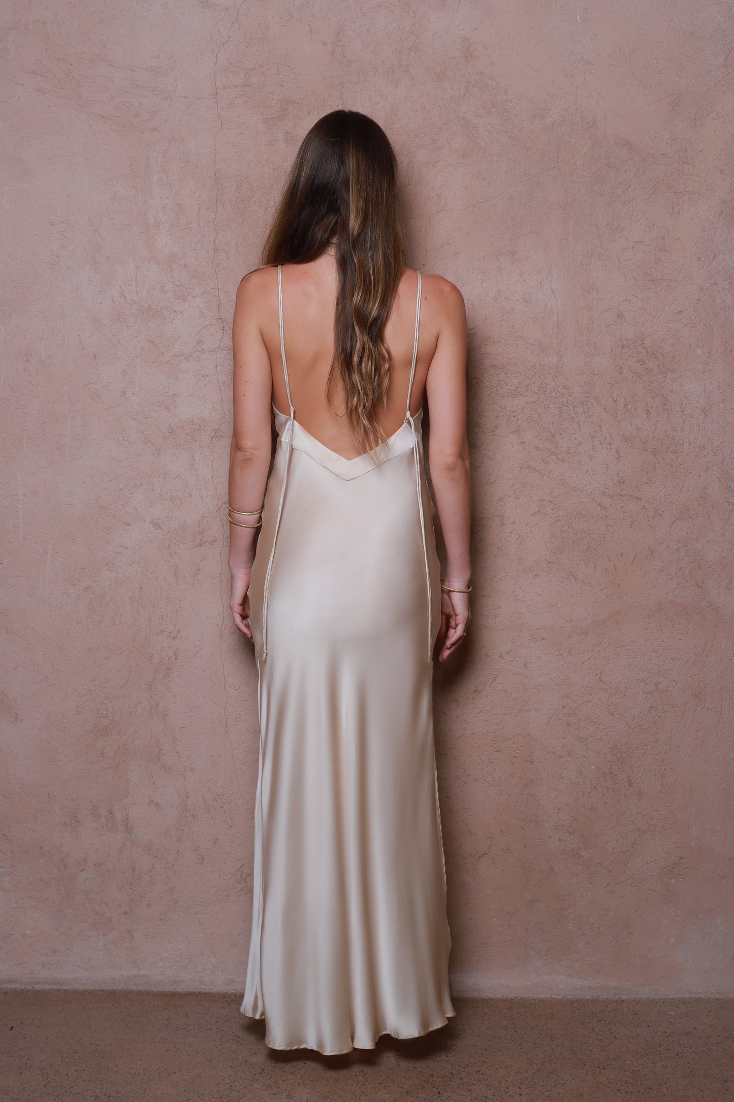 Woman wearing a long, light-colored silk dress against a pink wall.