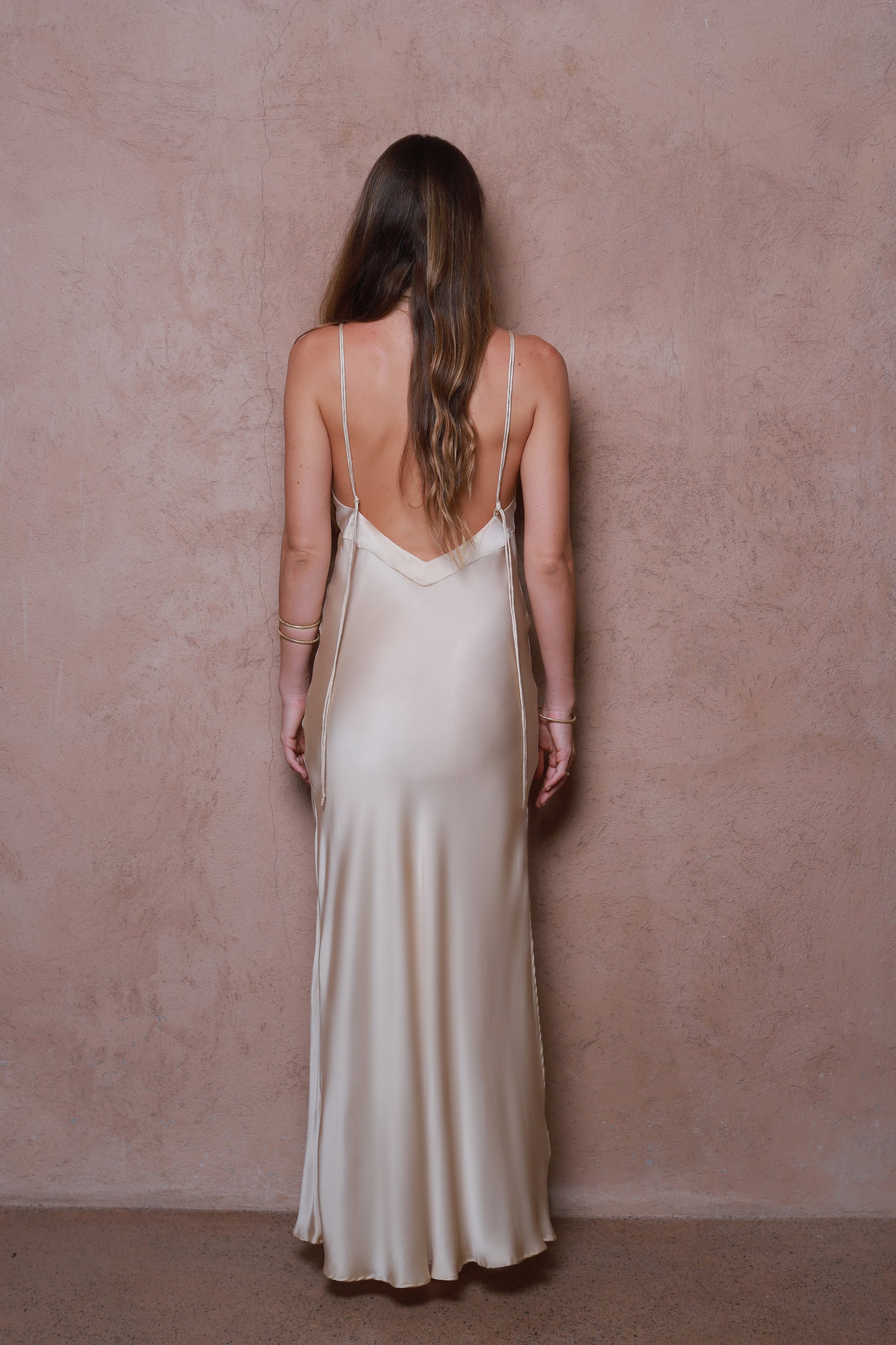 Woman wearing a long, light-colored silk dress against a pink wall.