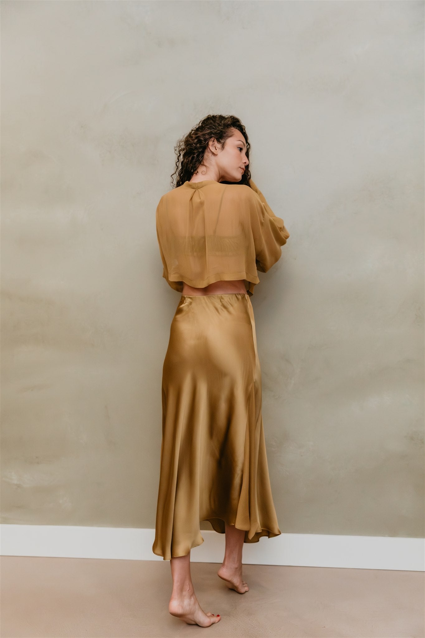 Woman wearing a brass outfit against a plain wall