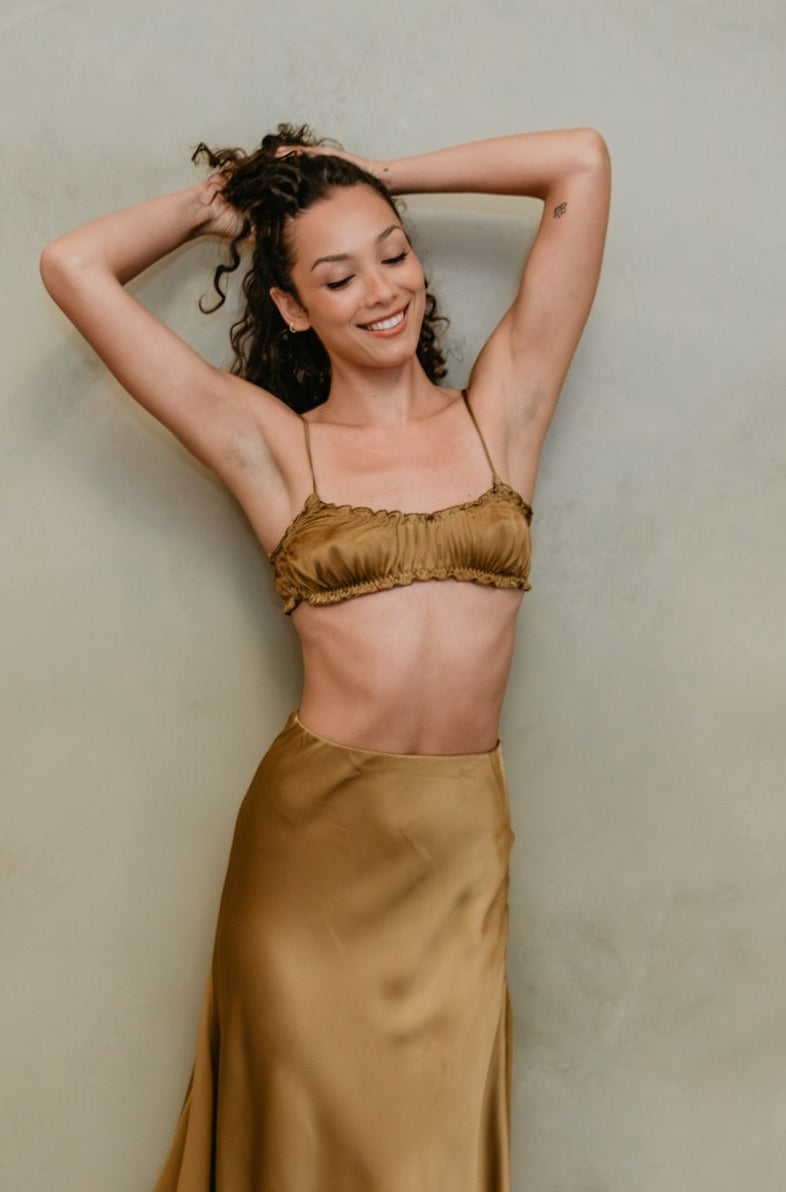 Woman wearing a gold satin skirt and top against a beige wall.