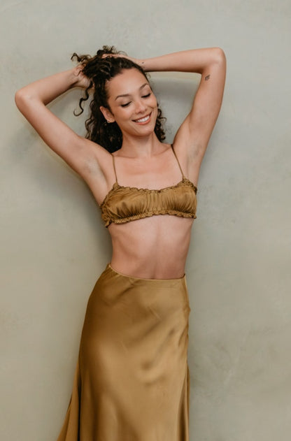Woman wearing a gold satin skirt and top against a beige wall.