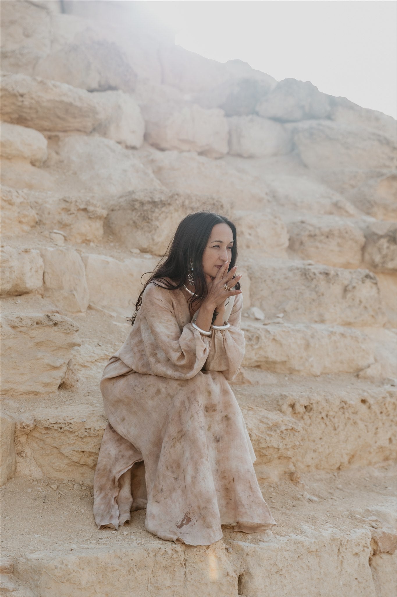 Woman in a beige dress sitting on stone steps with a mountainous background