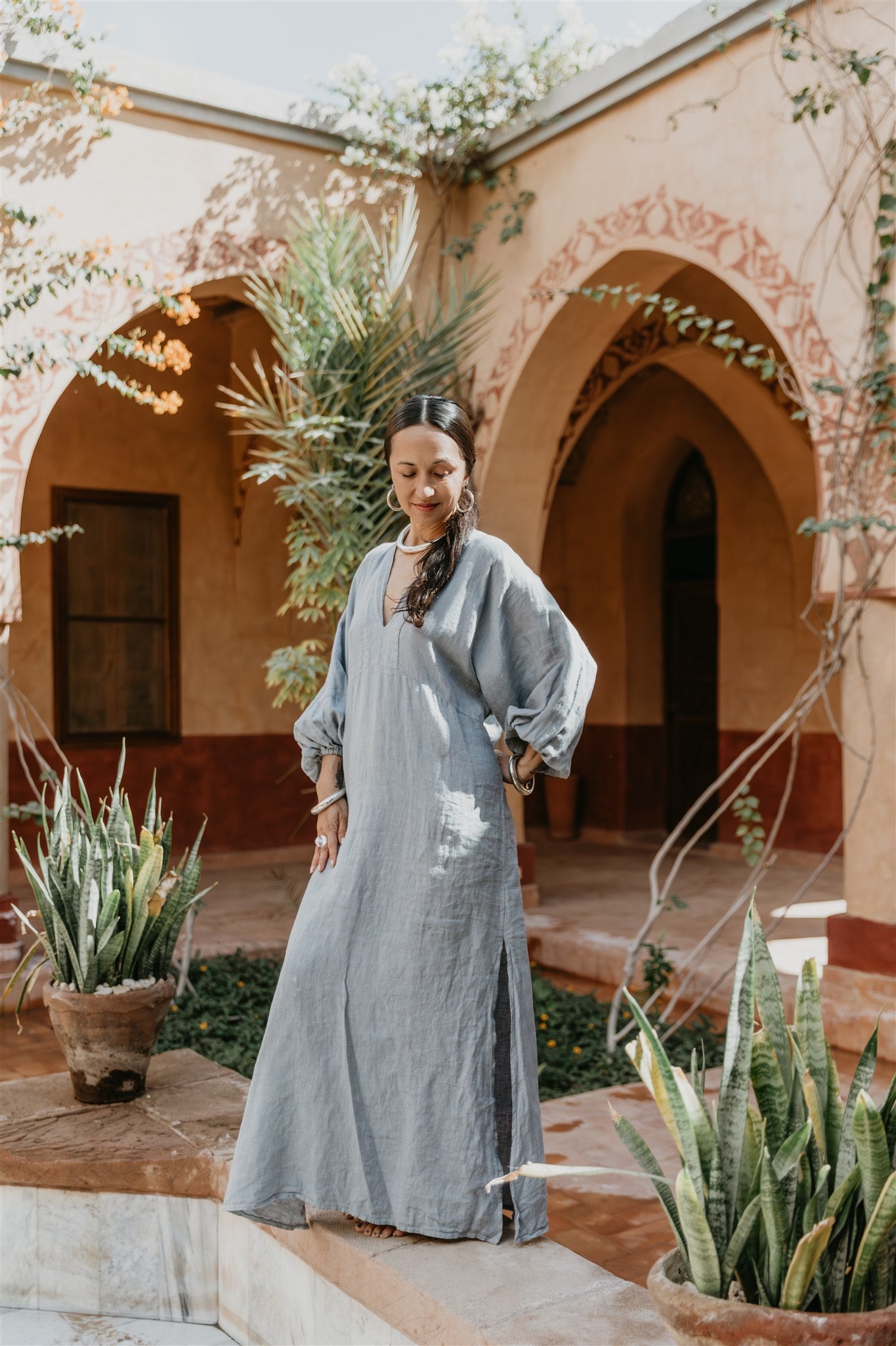 Woman in a long light blue dress standing in a courtyard with arches and plants in Egypt.