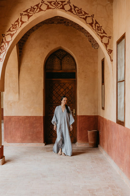 Woman in a long dress standing in a room with arched doorways and decorative walls.