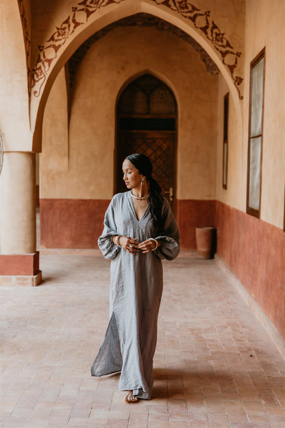 Woman in a long, light-colored dress standing in a sunlit hallway with arches in Egypt.