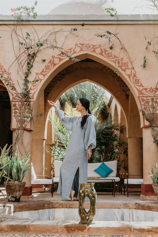 Woman in a blu linen kaftan dress standing in a decorative outdoor setting with arches and plants in Egypt 
