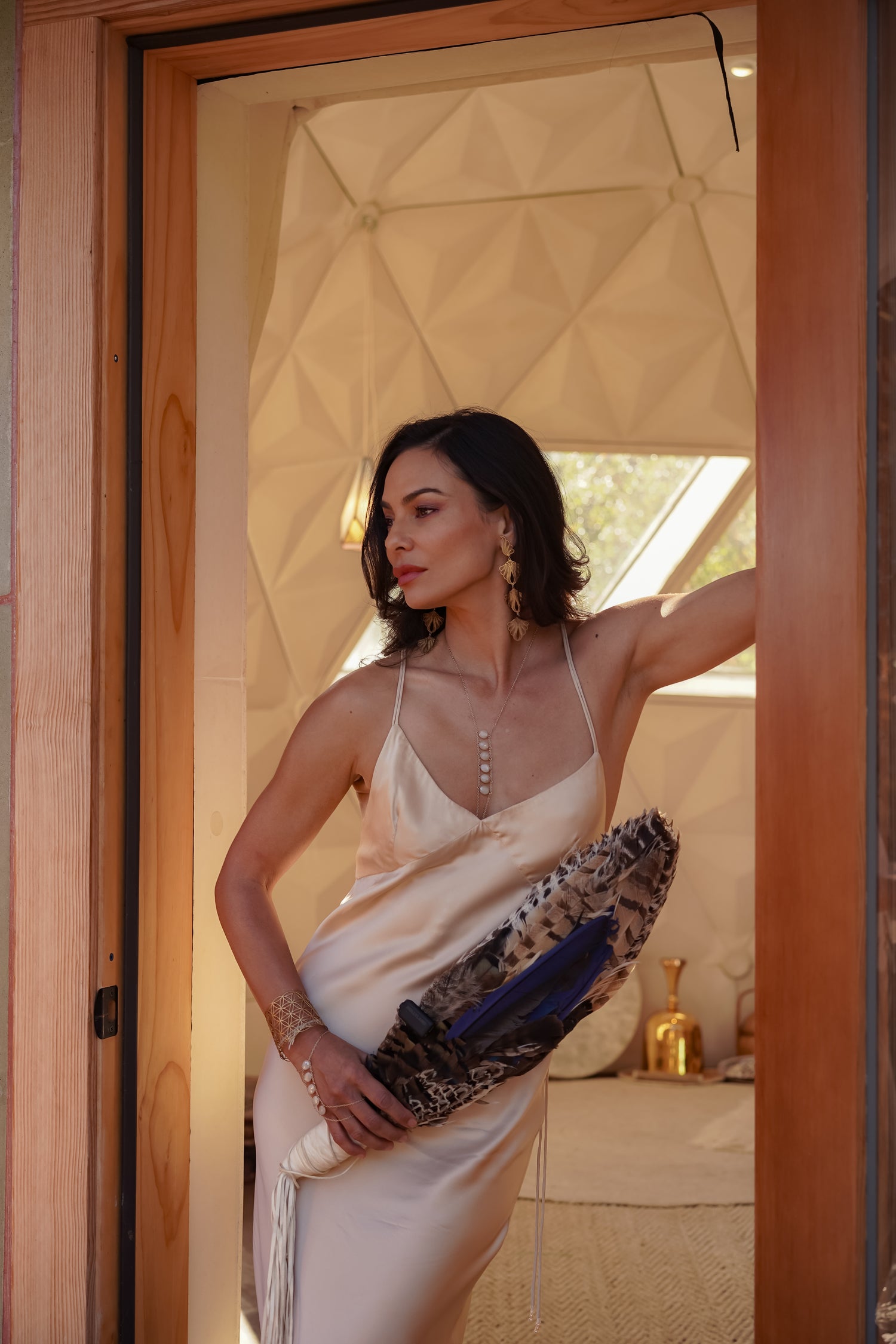 Woman in silk slip dress holding a clutch, standing in a doorway.