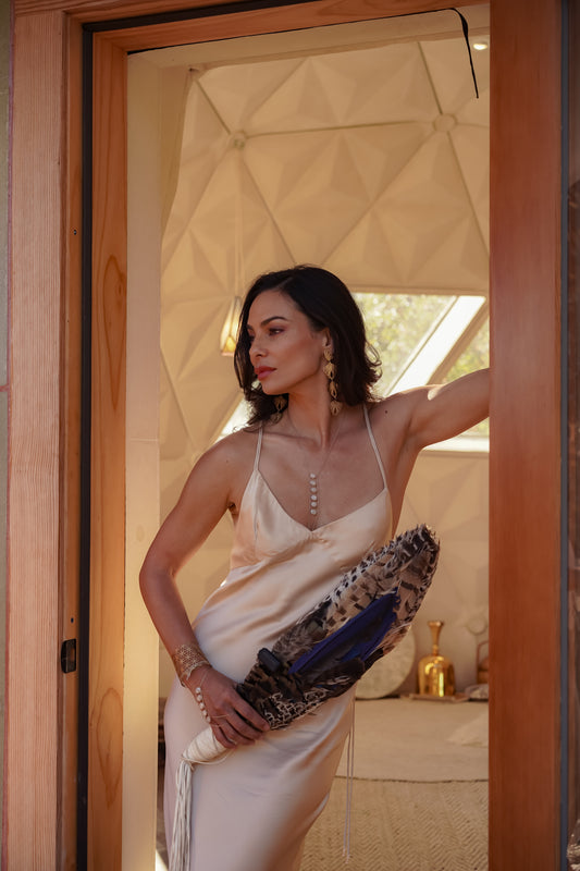 Woman in silk slip dress holding a clutch, standing in a doorway.
