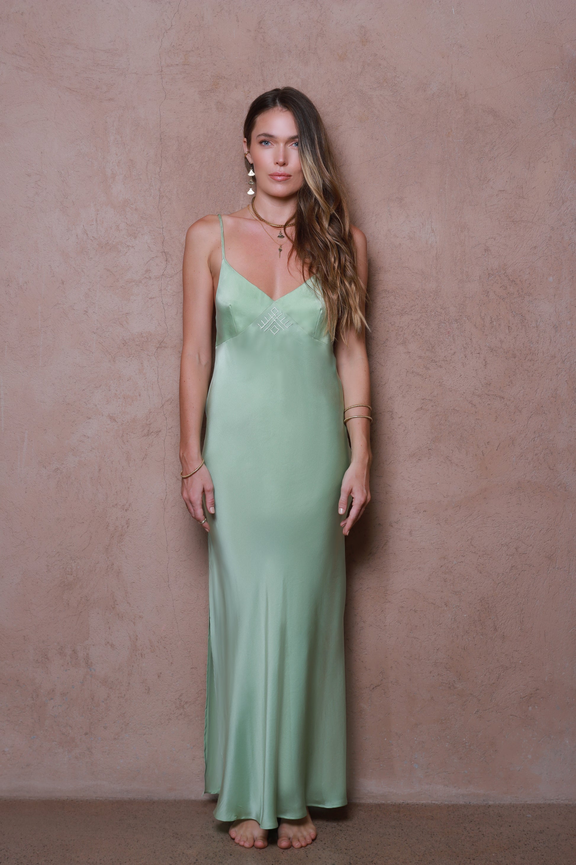 Woman wearing a green slip dress against a beige wall