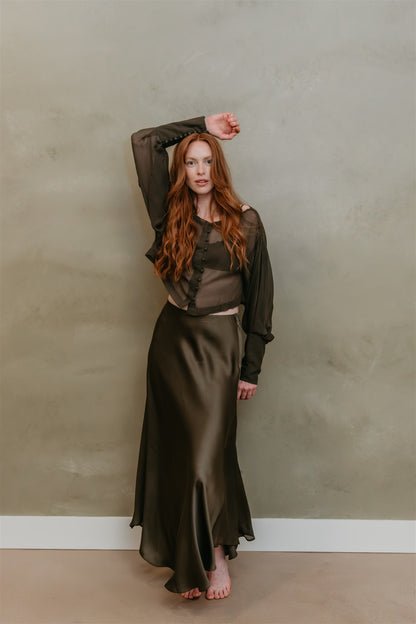 Woman in a long, dark green skirt standing against a plain wall.
