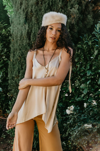 Woman wearing a beige top and pants with a fur hat in a garden setting