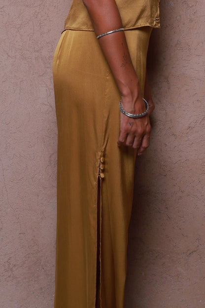 Person wearing a gold color silk matching  outfit standing in front of a beige wall.