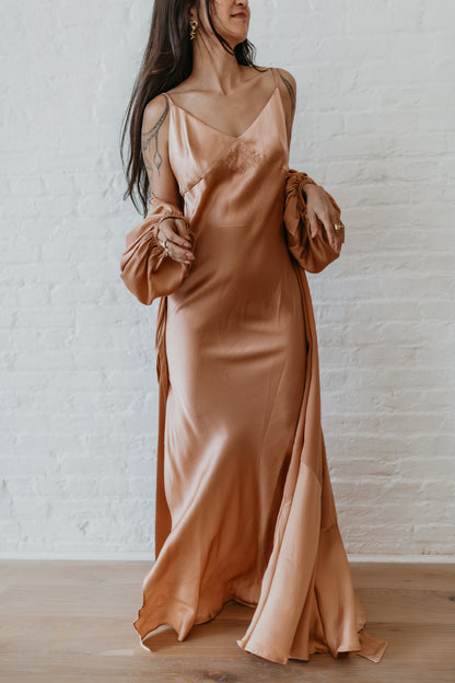 Woman wearing a long, flowing dress with ruffled sleeves against a white brick wall.