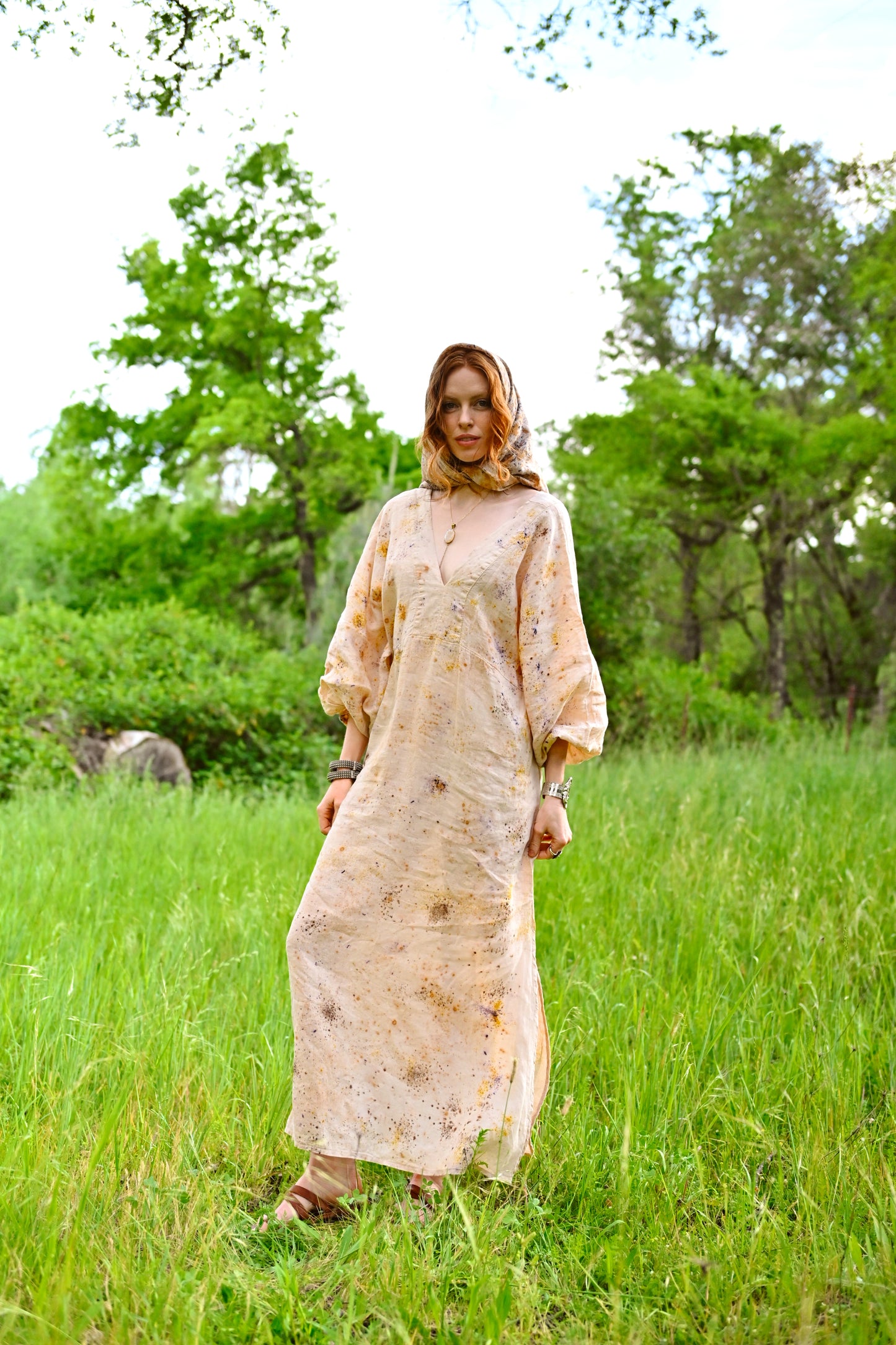 Model wearing The Flora Dress in botanical-dyed linen with attached hood, full-length view standing in green meadow, Payet Maison Founder's Collection
