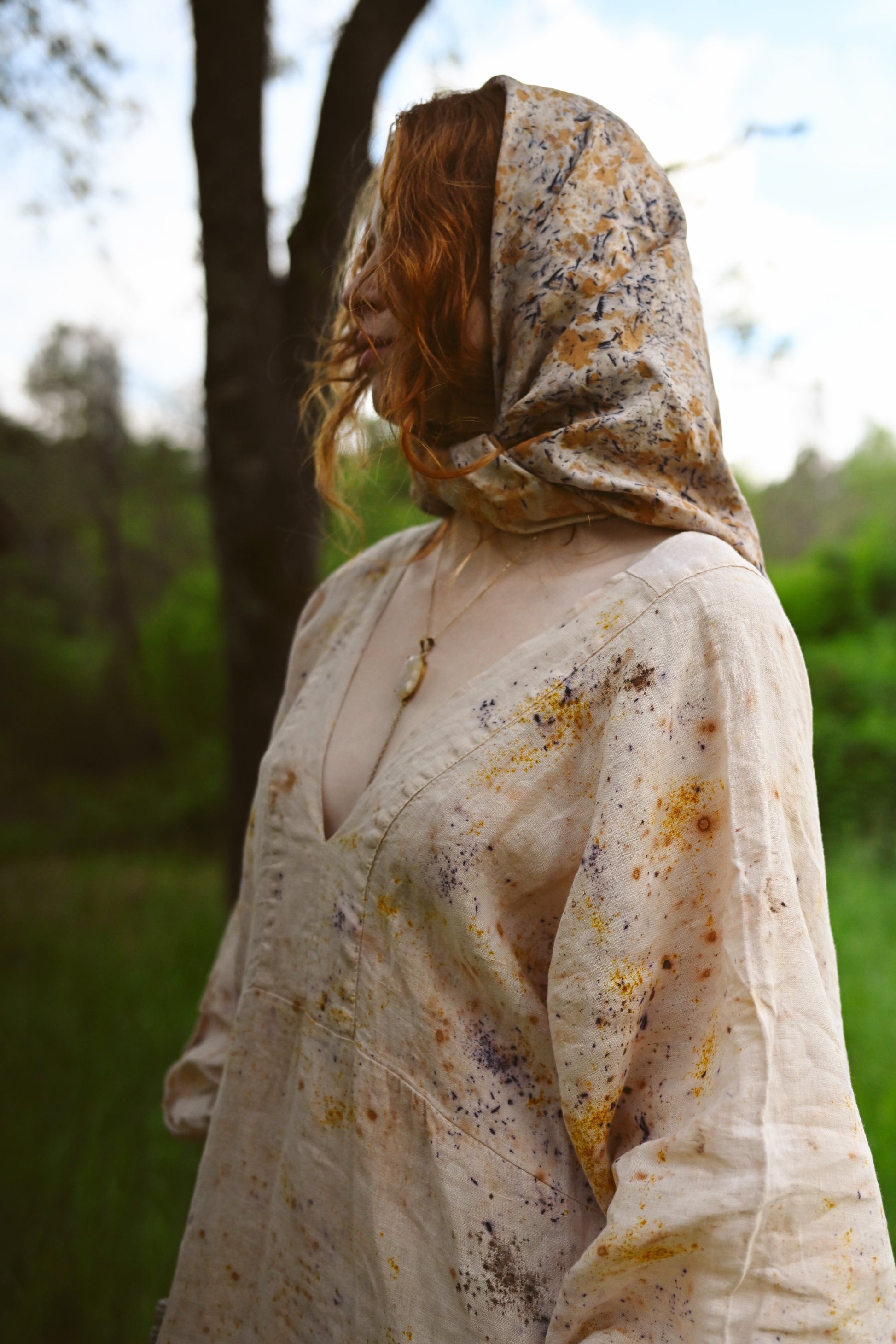 Model wearing The Flora Dress in botanical-dyed linen with attached hood, full-length view standing in green meadow, Payet Maison Founder's Collection