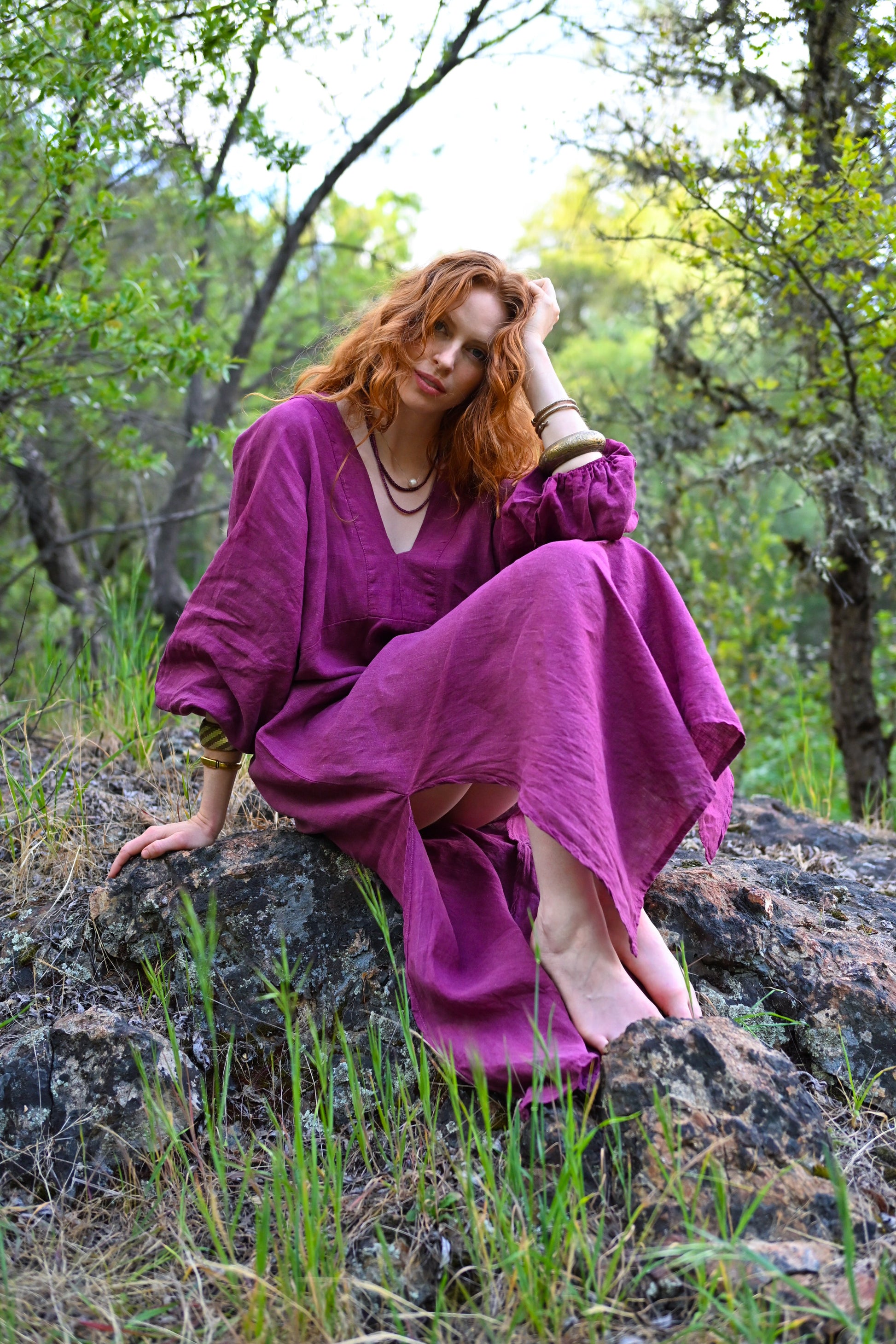 Woman in a purple dress sitting on a rock in a forest