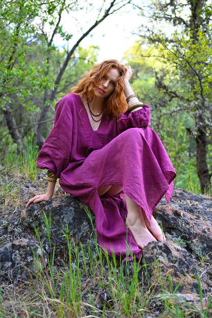 Woman in a purple dress sitting on a rock in a forest
