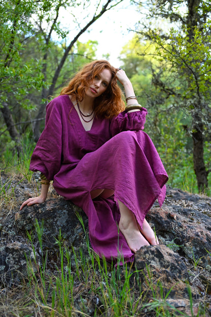 Woman in a purple dress sitting on a rock in a forest