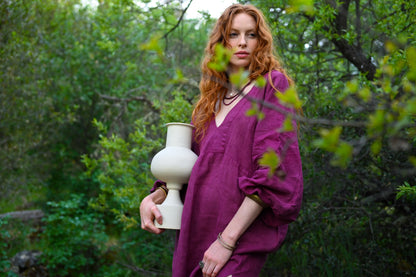 Model wearing The Terra Dress in plant-dyed plum linen holding ceramic vase in woodland setting, Payet Maison Founder's Collection