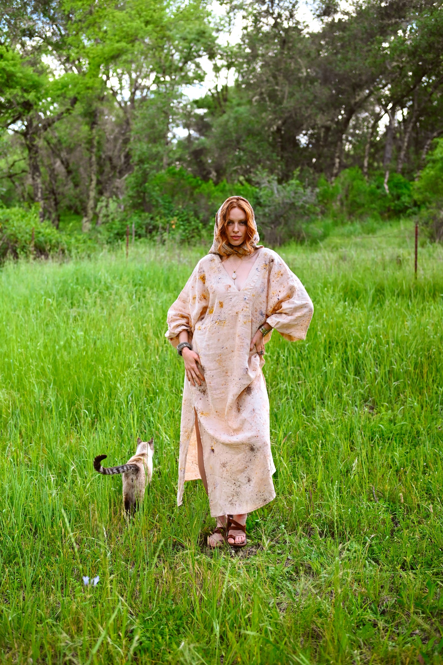 Full-length styled shot of model in botanical-dyed hooded linen dress with pendant necklace in green meadow, Payet Maison Founder's Collection