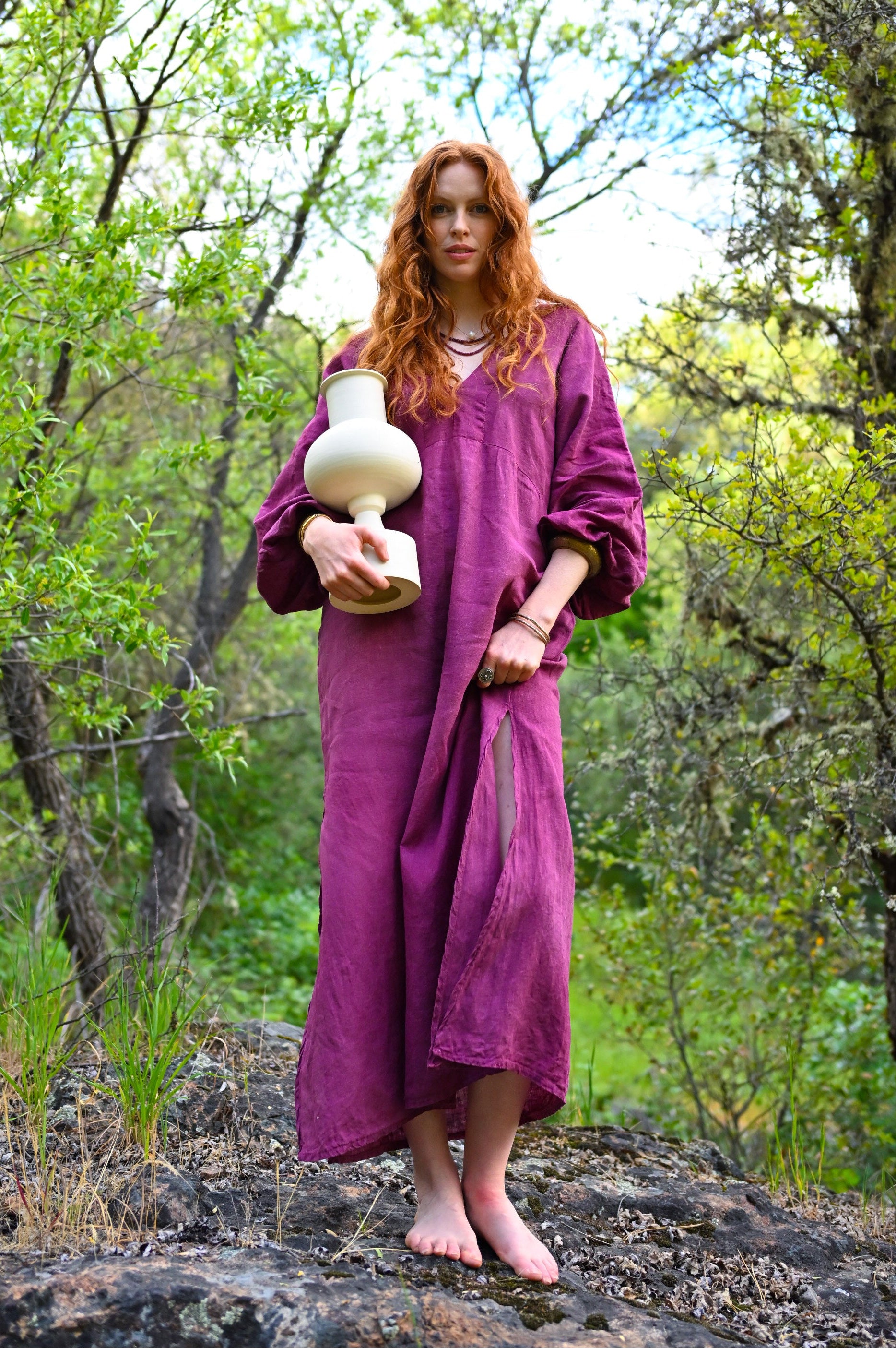 Plant-dyed linen dress in deep plum by Payet Maison, full-length front view with deep V-neckline and relaxed flowing silhouette in woodland setting

