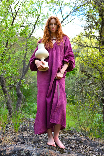 Plant-dyed linen dress in deep plum by Payet Maison, full-length front view with deep V-neckline and relaxed flowing silhouette in woodland setting
