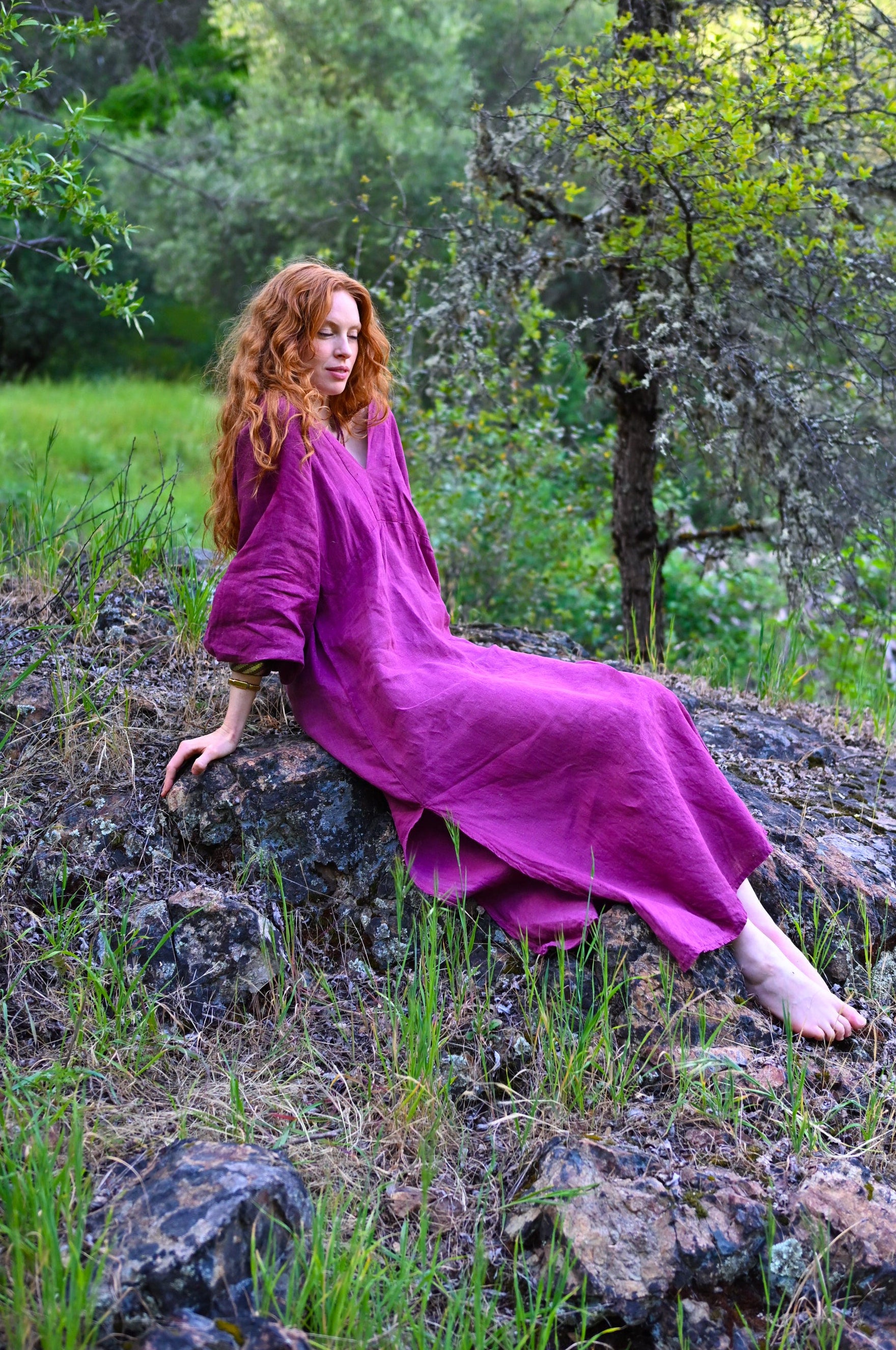 Ankle-length hem with side slit detail on The Terra Dress, plant-dyed linen in deep plum, bare feet on forest floor
