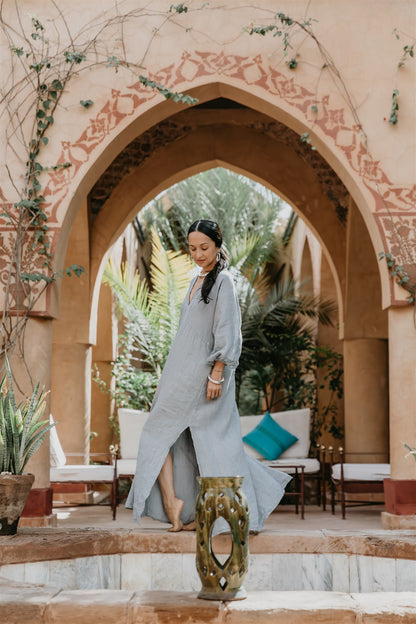 Woman in a long blue dress standing under an ornate archway in a garden setting.