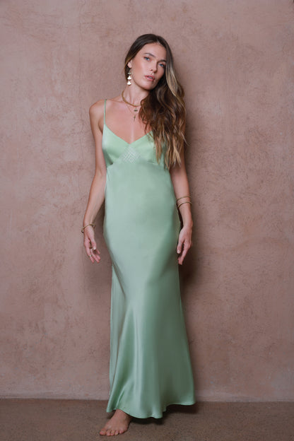 Woman wearing a light green slip dress against a beige wall