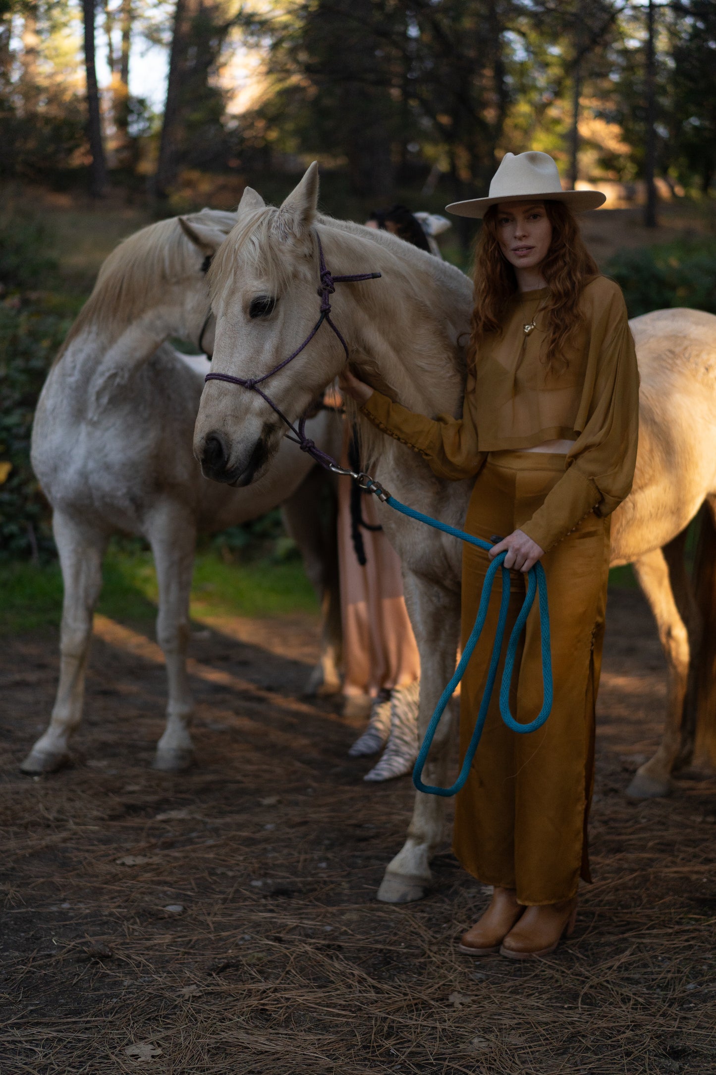 Woman in a gold outfit standing next to a white horse in a forest setting
