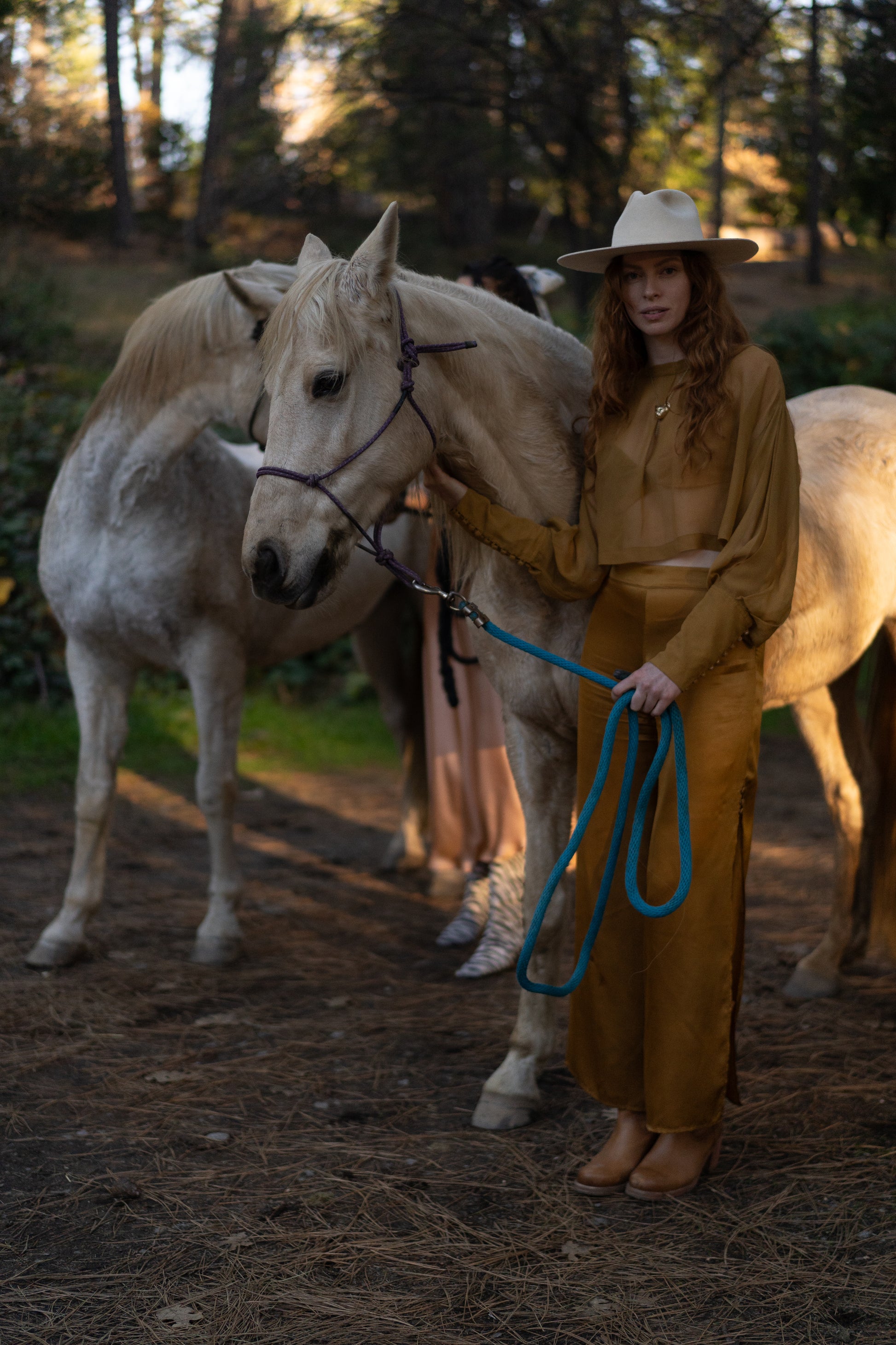 Woman in a gold outfit standing next to a white horse in a forest setting
