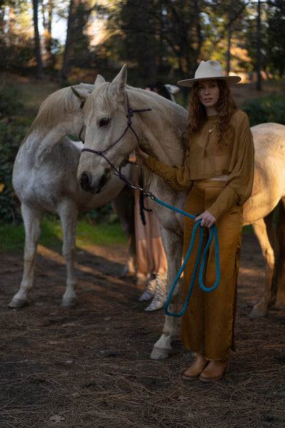 Woman in a gold outfit standing next to a white horse in a forest setting